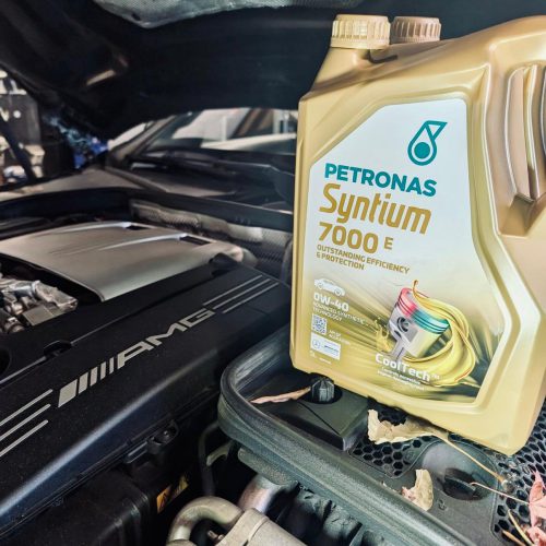 Foto van een technicus die een auto onderhoudt met Petronas motorolie, waarbij de motor zorgvuldig wordt gecontroleerd en gevuld tijdens de onderhoudsbeurt.